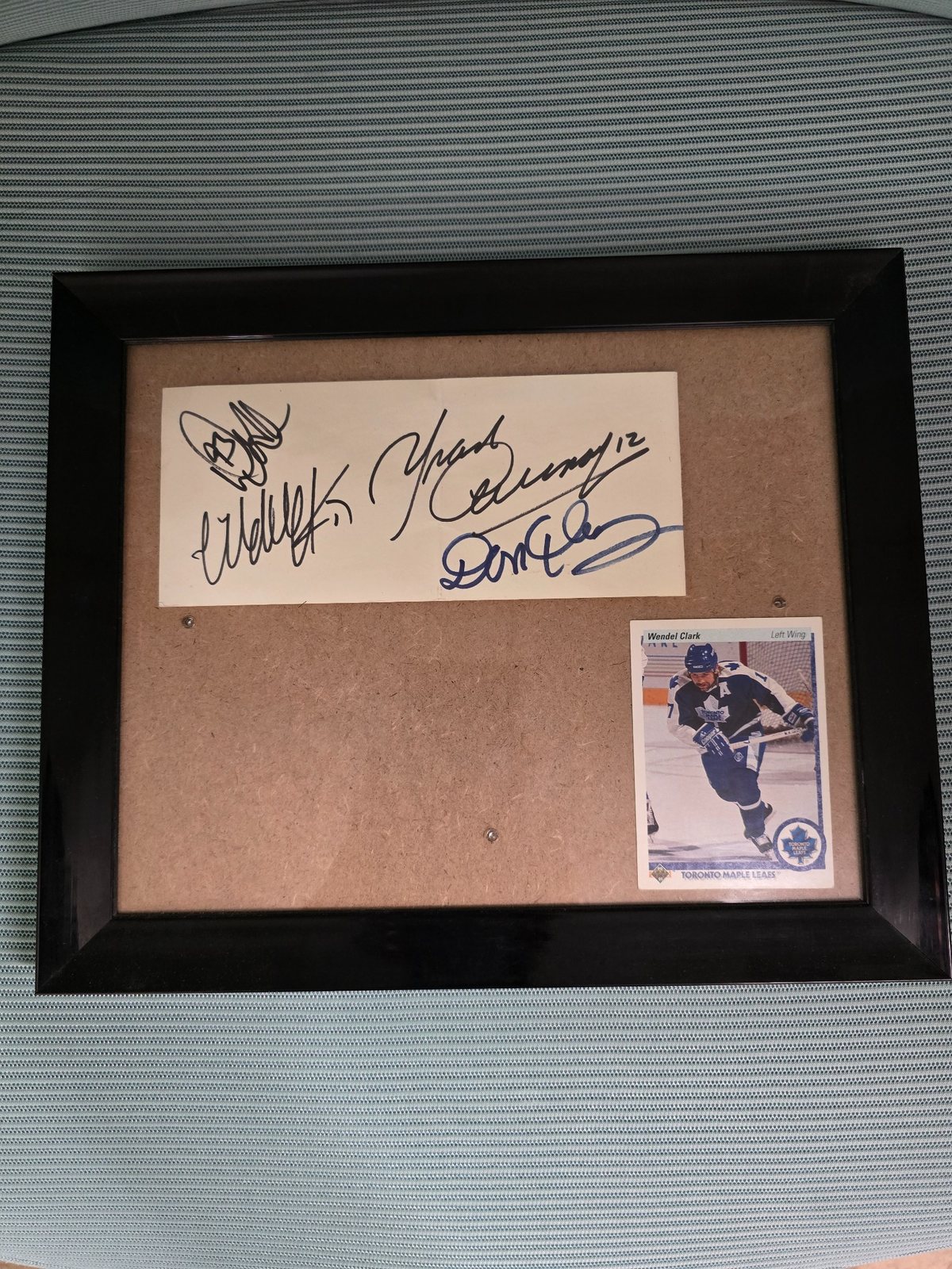 Framed display containing several autographs on a white ticket stub and a Wendel Clark hockey card.