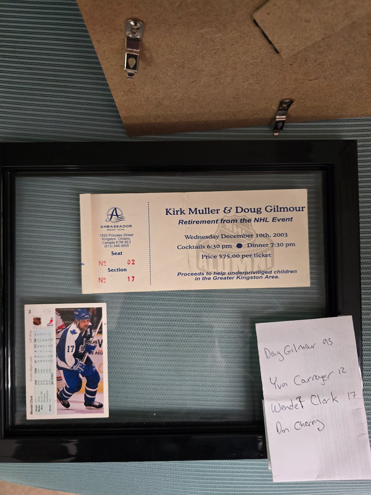Open frame showing a 2003 Kirk Muller and Doug Gilmour retirement event ticket, a Wendel Clark hockey card, and a handwritten list of autographs.