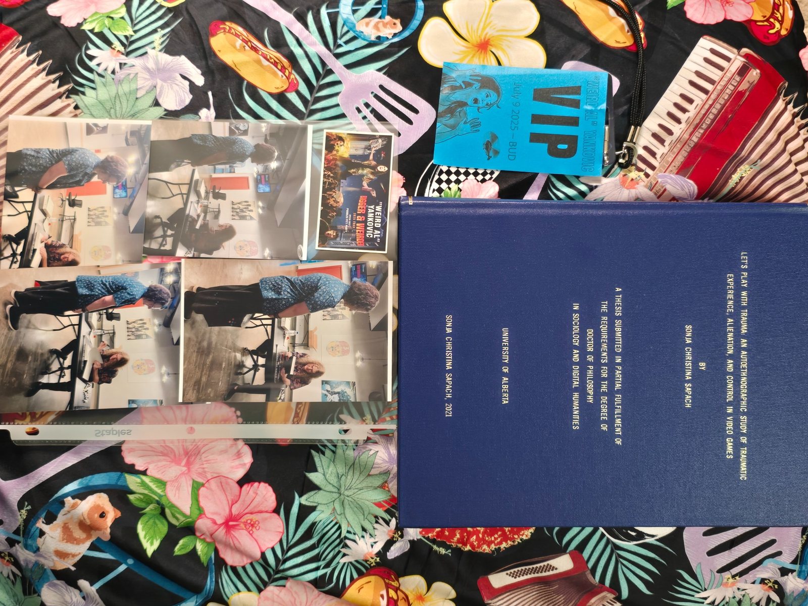 Bound dissertation, VIP pass, concert photos, and lanyard arranged on a patterned cloth with music-themed illustrations.