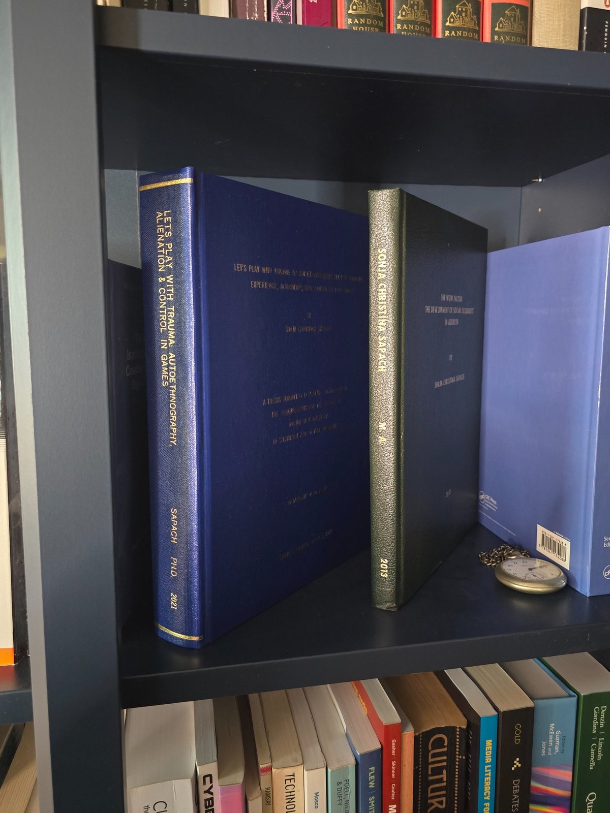 Bound blue doctoral dissertation standing on a dark bookshelf beside other academic books.