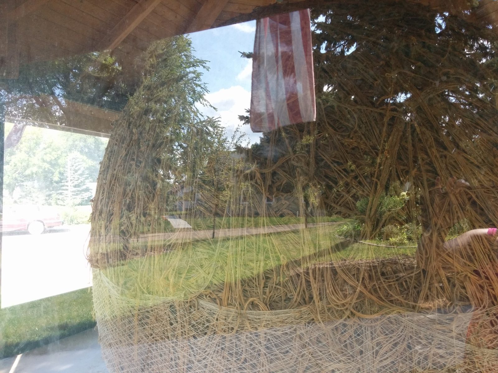 Close view through glass of the large Darwin ball of twine, showing dense layers of brown twine, an American flag, and reflections from the surrounding park.