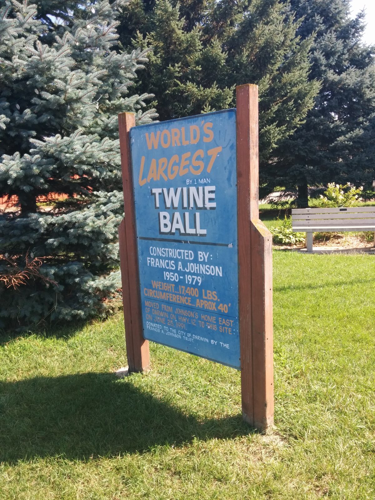 A blue outdoor sign in Darwin, Minnesota reading World's Largest by 1 Man Twine Ball and listing Francis A. Johnson, 1950–1979, weight 17,400 pounds, and circumference approximately 40 feet.