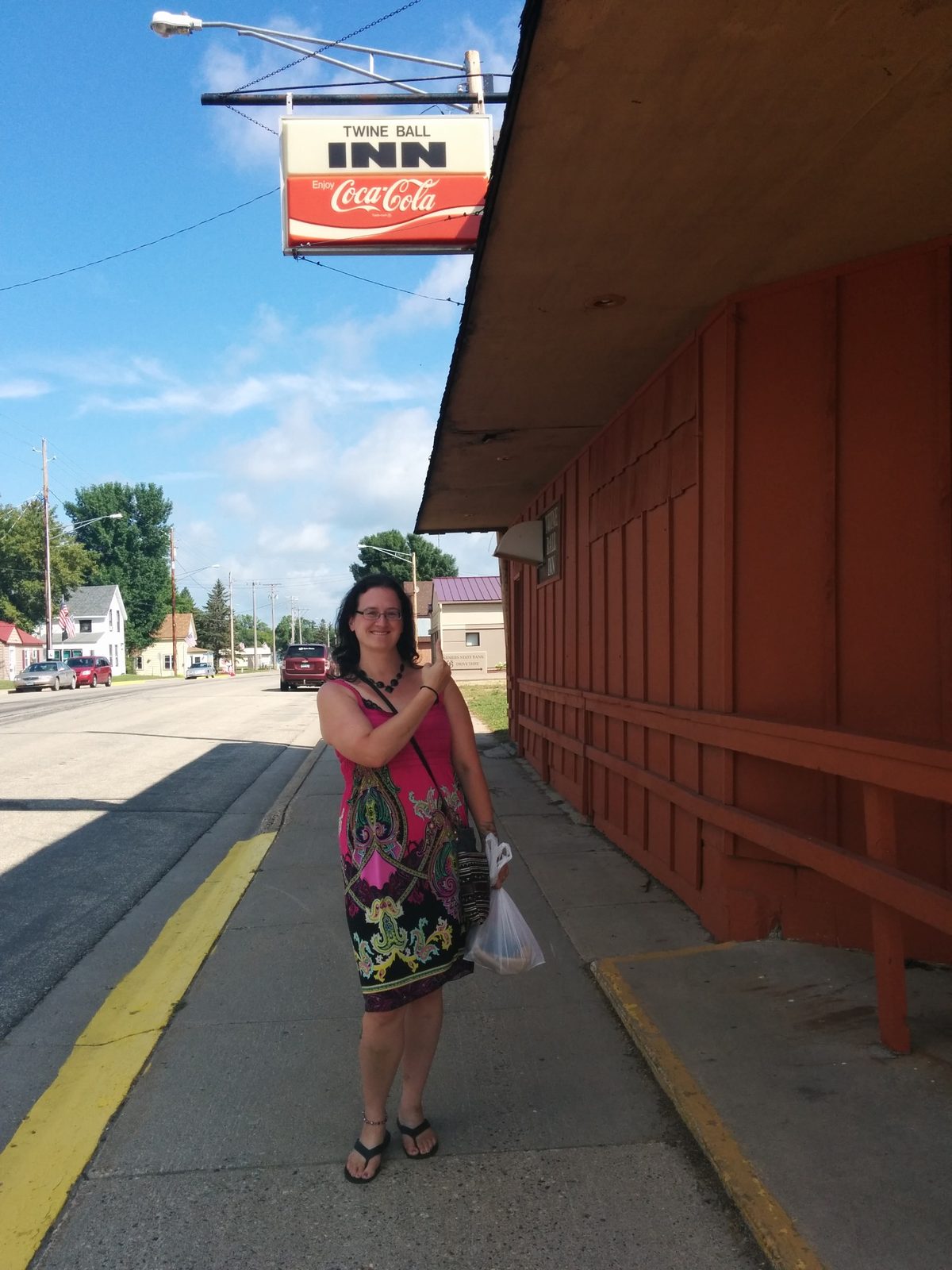 Sonja standing on a sidewalk beside a red building beneath a hanging sign reading Twine Ball Inn.
